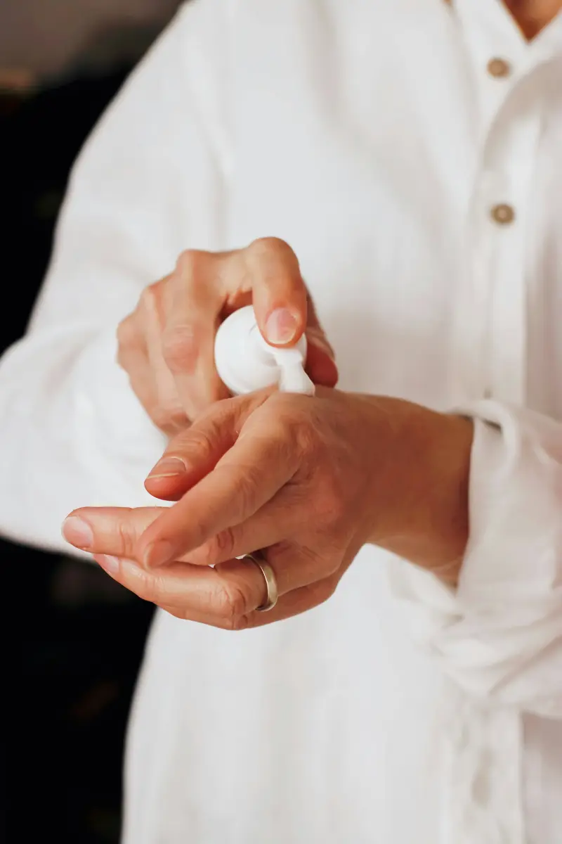 Zwei Hände verteilen Creme, dahinter ein weißes Leinenhemd