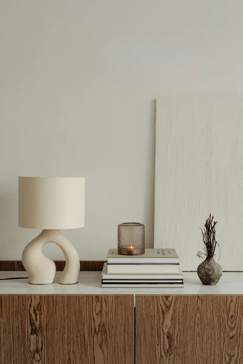 Heller Raum mit Keramiklampe, Büchern und einer Vase auf einem Holzsideboard