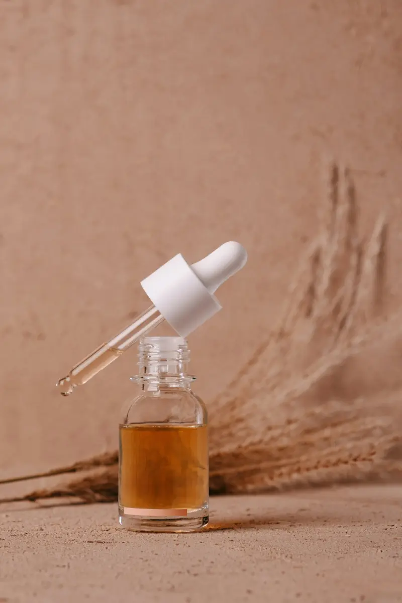 Ein Glasfläschchen mit Pipette und bernsteinfarbenem Serum vor zartem Nude