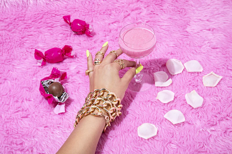 Hand mit goldenem Schmuck und hellen Nägeln auf rosa Plüsch
