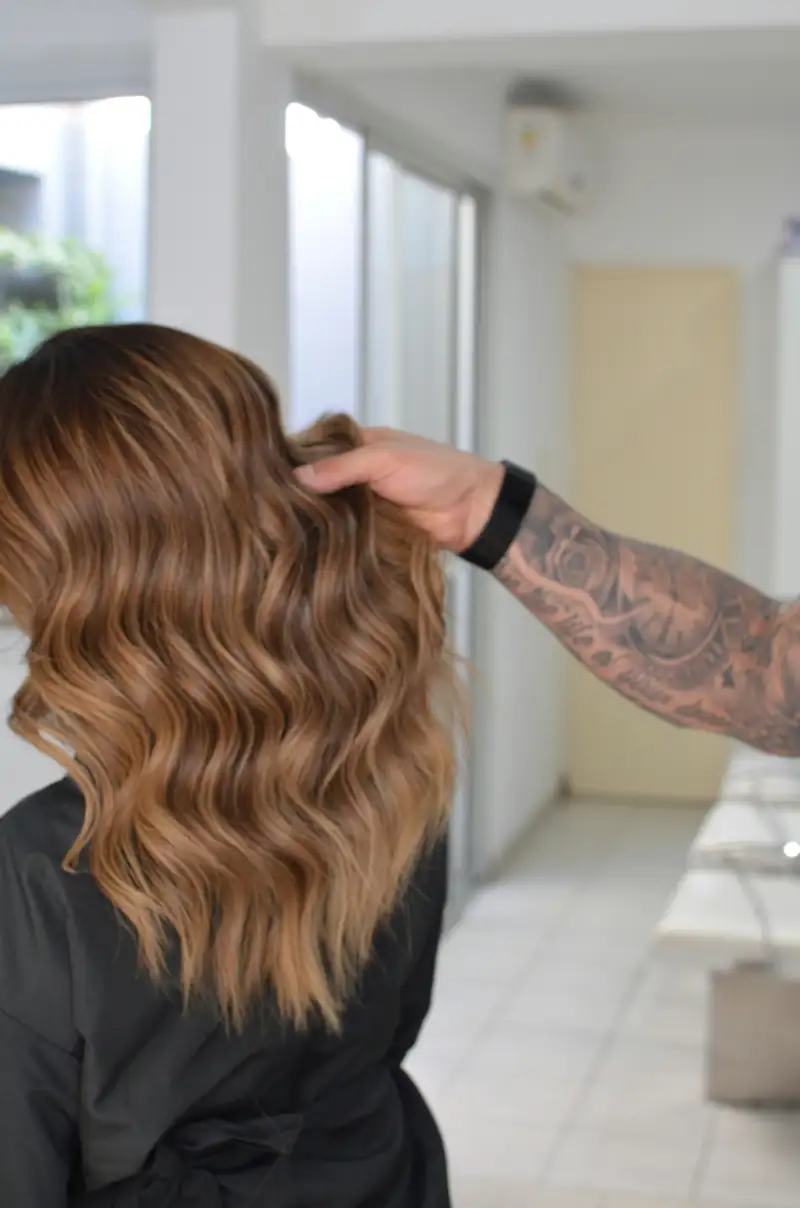 Eine Friseurin hebt schulterlange Wellen mit Balayage in Karamell und Honig an