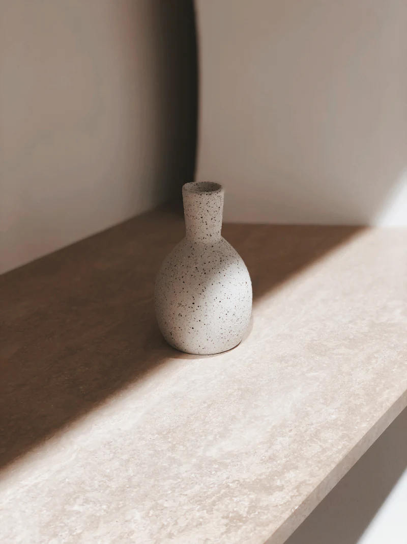 Eine helle Vase aus Steinzeug auf einem Regal im Streiflicht